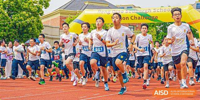 A group of older students wearing white and blue running bibs competing in a race on an outdoor track at Sedbergh School Fuzhou.