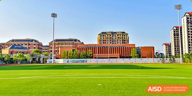 The traditional red brick academic buildings of Sedbergh School Fuzhou standing tall behind a bright green sports field.