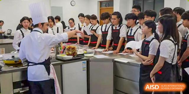 Students wearing aprons and school shirts participate in a hands-on cooking or health and nutrition class at Sedbergh School Fuzhou.