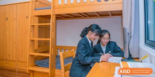 Two female students in school uniform studying together at a desk inside a comfortable student dormitory room at Sedbergh School Fuzhou.