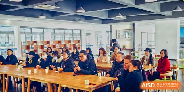 Wenzhou No.22 Senior Middle School students and adults gathered around wooden tables in a brightly lit common area for a meeting or group discussion.