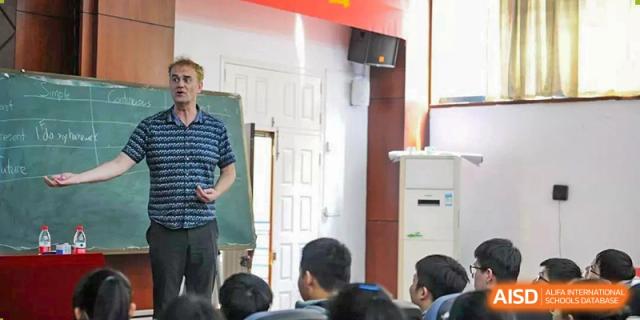 An instructor at Wenzhou No.22 Senior Middle School giving a presentation or lecture to a class, standing near a projector screen.