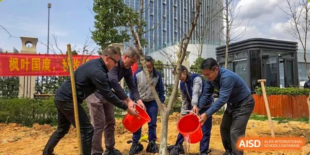 Wenzhou No.22 Senior Middle School teachers and students participating in a tree planting activity, watering a newly planted sapling outdoors.