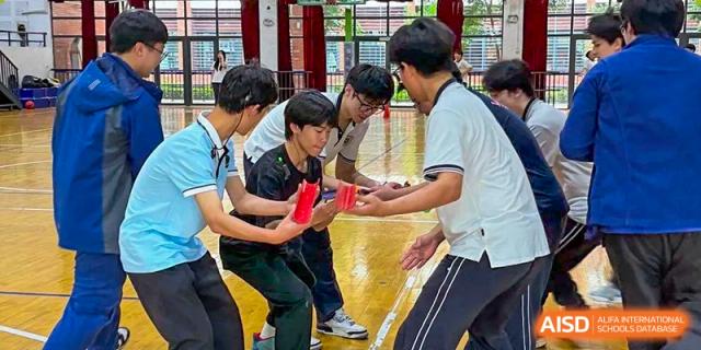 Wenzhou No.22 Senior Middle School students participating in an indoor teamwork game, balancing a red object between them.