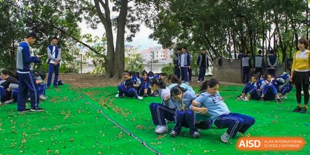 Group of Wenzhou No.22 Senior Middle School students sitting on the grass under trees during an outdoor activity or team-building exercise.