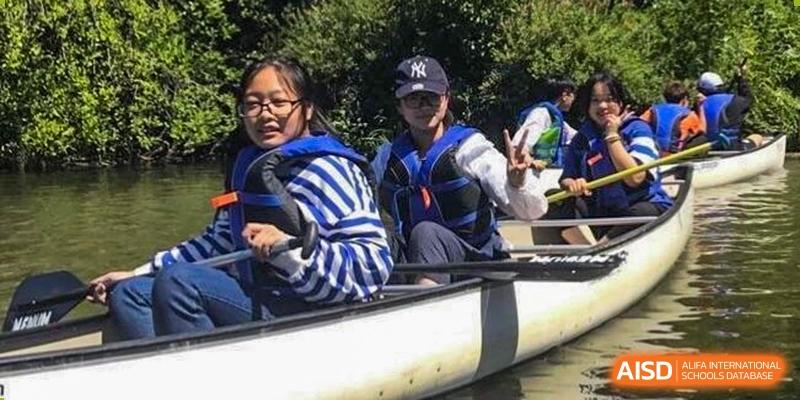 Wenzhou No.22 Senior Middle School students wearing life vests while canoeing or kayaking on the water, smiling and posing for a photo.