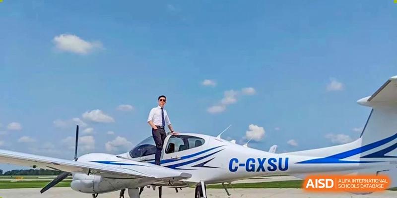 Wenzhou No.22 Senior Middle School student in a suit standing on the wing of a small white private airplane, under a bright blue, cloudy sky.