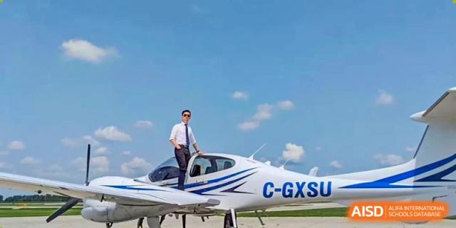 Wenzhou No.22 Senior Middle School student in a suit standing on the wing of a small white private airplane, under a bright blue, cloudy sky.