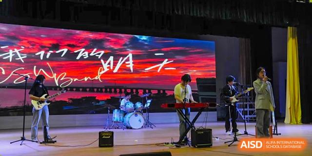 Wenzhou No.22 Senior Middle School student band performing on stage, with a keyboardist and drummer in front of a large, vibrant LED screen.