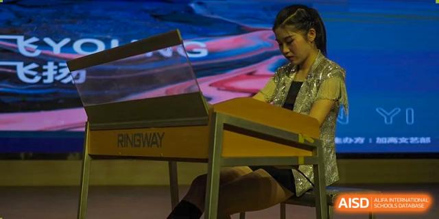 Wenzhou No.22 Senior Middle School student sitting at a desk, focused on playing the piano or keyboard in a brightly lit room or stage area.