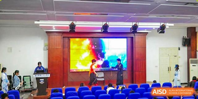 Two Wenzhou No.22 Senior Middle School students giving a musical performance on stage, with a large colorful screen behind them and rows of blue audience seating.