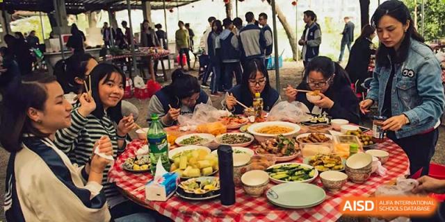 Students from Wenzhou No.22 Senior Middle School gathered around a table with a red and white checkered tablecloth, enjoying a large outdoor meal together.