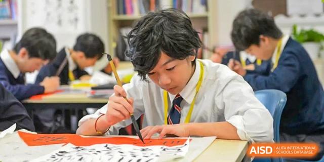 A male student from Dulwich International High School Programme Hengqin (DHHQ) focused on practicing Chinese calligraphy with a brush and ink.