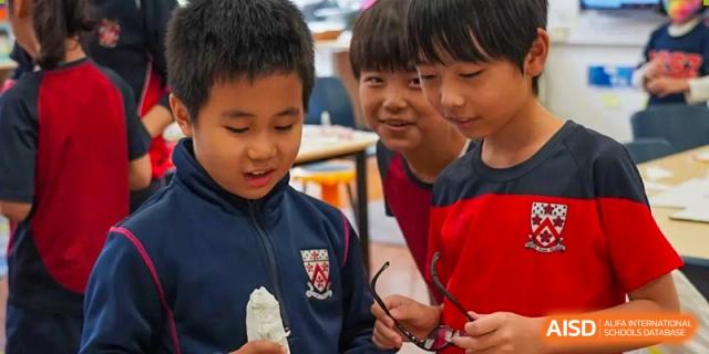 Three students from Dulwich International High School Programme Hengqin (DHHQ) collaborating and looking at a small object together, demonstrating teamwork.