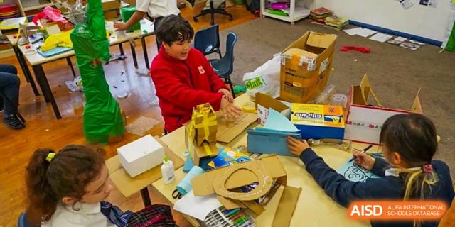 Students from Dulwich International High School Programme Hengqin (DHHQ) working on a creative construction project using cardboard and various materials in a workshop setting.