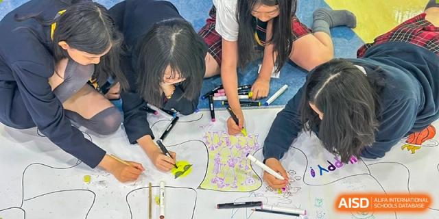 Students from Dulwich International High School Programme Hengqin (DHHQ) collaborating to draw or color on a large piece of paper on the floor.