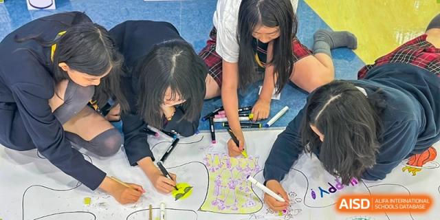 Two female students from Dulwich International High School Programme Hengqin (DHHQ) drawing together on a large sheet of paper on the ground, likely as a collaborative art assignment.
