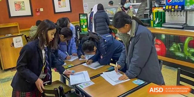Students from Dulwich International High School Programme Hengqin (DHHQ) gathered around a table, actively studying or completing paperwork in a communal area.
