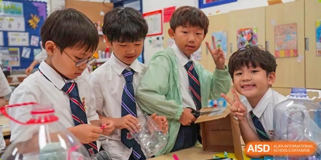 Three young male students from Dulwich International High School Programme Hengqin (DHHQ) collaborating on a small project in the classroom, with one student giving a peace sign.