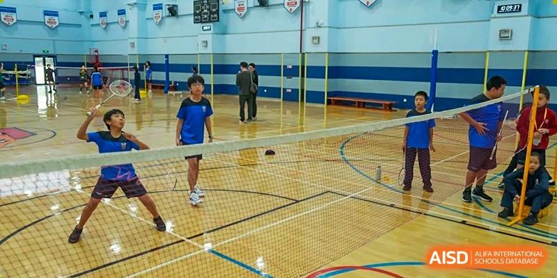 Students from Dulwich International High School Programme Hengqin (DHHQ) playing badminton on an indoor court with a net visible.