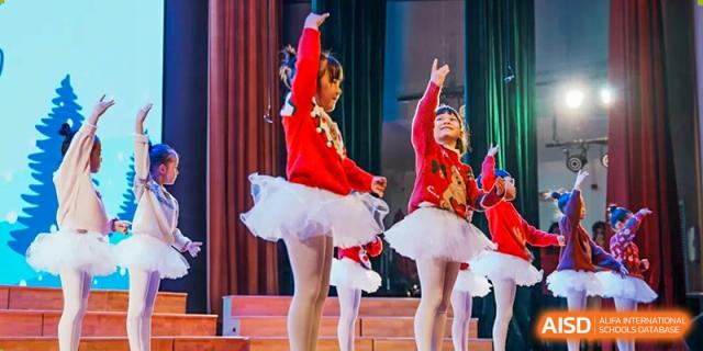 Young students from Dulwich International High School Programme Hengqin (DHHQ) performing a ballet or classical dance in red costumes with tutus on a stage.