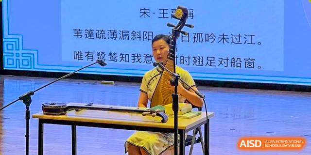 A student from Dulwich International High School Programme Hengqin (DHHQ) playing a traditional Chinese string instrument (likely an Erhu or Guzheng) during a performance.