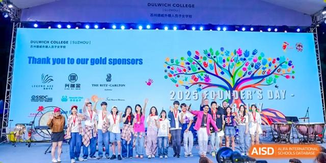 A group of students and teachers from Dulwich International High School Programme Hengqin (DHHQ) on stage at a "2023 FUND..." event, acknowledging their gold sponsors.