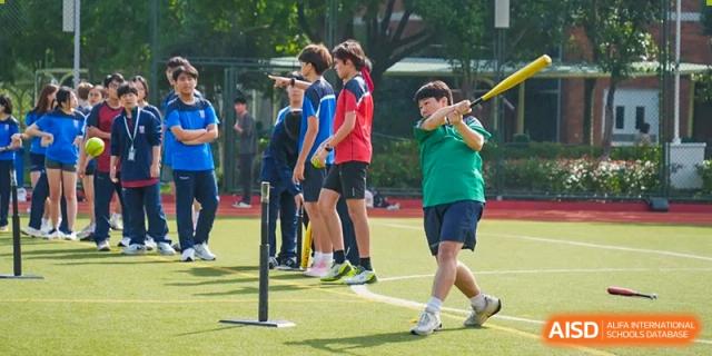 A male student from Dulwich International High School Programme Hengqin (DHHQ) taking a swing with a bat at a yellow ball during a school sports class.