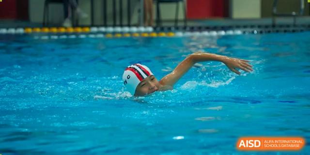 A student from Dulwich International High School Programme Hengqin (DHHQ) swimming in a competition or practice, with only the arm and head visible above the water.