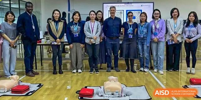A group of students and teachers from Dulwich International High School Programme Hengqin (DHHQ) standing behind a training instructor who is demonstrating CPR on a mannequin.