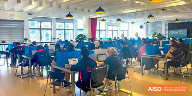 Older students sitting at tables, working quietly on laptops during a study period at Shekou International School.