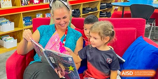 A teacher reading a book to two young, happy students in a cozy classroom at Shekou International School.