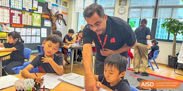 An elementary teacher assisting a young student with his work at a table during a class activity at Shekou International School.