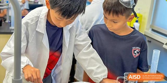 Two young boys working together on a science experiment while one wears a lab coat at Shekou International School.