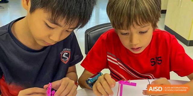 Two elementary students focused on building a small object with components in a classroom at Shekou International School.
