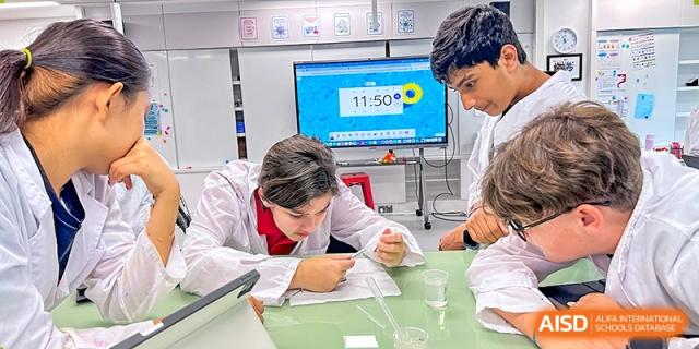 A student in a lab coat performing a precise science experiment in front of a digital display at Shekou International School.