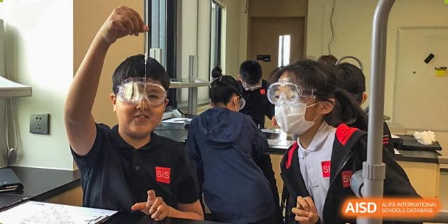 Students wearing goggles and lab coats working on a project during a high school science class at Shekou International School.