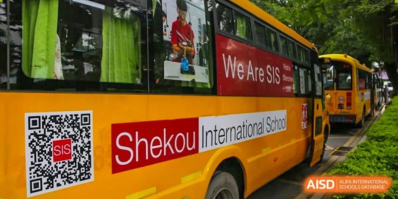 A close-up view of the side of a yellow bus clearly displaying the school's name: 'Shekou International School' and a red banner.