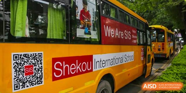 A close-up view of the side of a yellow bus clearly displaying the school's name: 'Shekou International School' and a red banner.