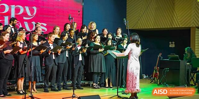 A choir performance is taking place on stage during a special event at Shekou International School, featuring many students.