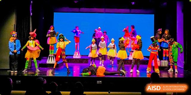 Students performing a vibrant dance routine on a brightly lit stage with a colorful backdrop at Shekou International School.