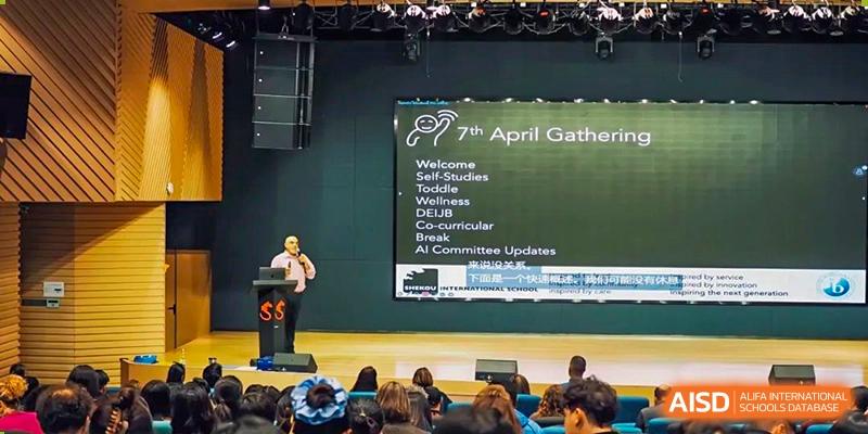 A speaker addresses an audience gathered in an auditorium at Shekou International School for the 7th April Gathering.