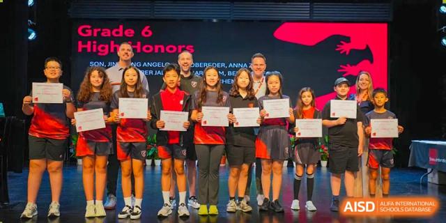 A group of high-achieving students from Shekou International School on stage with staff, proudly holding their academic honor certificates.