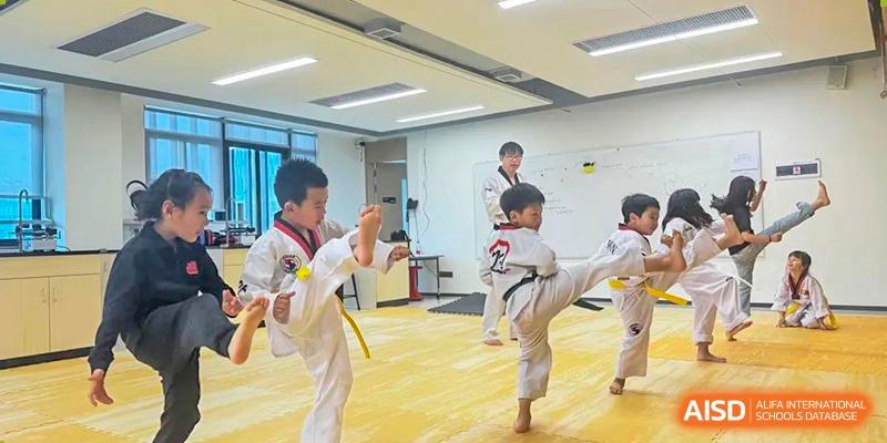 Young students practicing a high-kick martial arts maneuver during a Taekwondo class at Shekou International School.