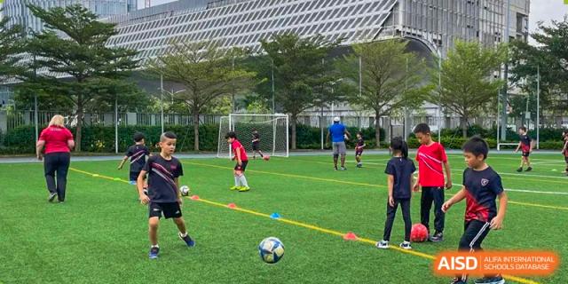 Students playing soccer/football on a large, well-maintained green sports field at Shekou International School.