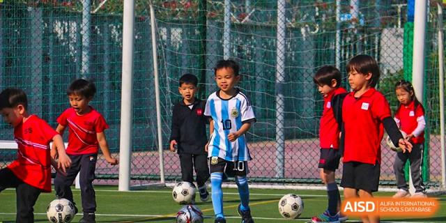 Two young boys in matching blue and white uniforms playing soccer/football on an outdoor turf at Shekou International School.
