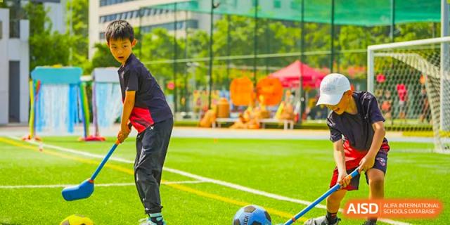A close-up of a student's legs and a soccer ball on the green turf field at Shekou International School during a sports training session.