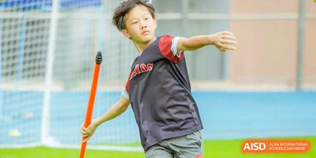 A student in a red and black shirt is actively participating in a running drill, holding an orange pole at Shekou International School.