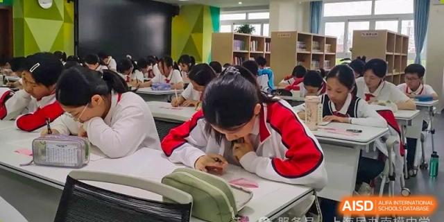 A close-up of a student in a red jacket focused intently on their desk work and writing in a bright classroom at Shanghai Nanyang Model Private School.