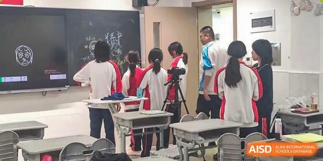 Students gathered around desks, possibly preparing for an activity or discussing a topic in a classroom at Shanghai Nanyang Model Private School.
